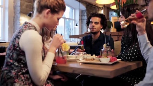 Happy multiethnic friends enjoying food drinks and holiday cheers at a restaurant