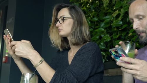 Young Couple Drinking Beverage and Using Smartphones in Cafe Addicted