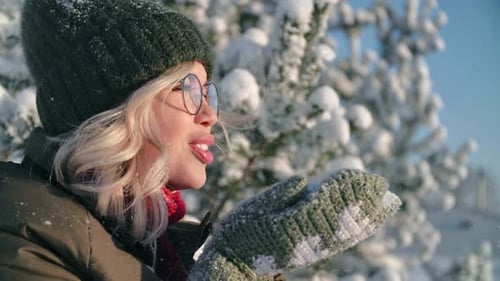 Portrait of Pretty Young Woman in Forest in Winter Day Girl Blowing Out Snow From Hands in Mittens