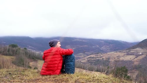 Young hiker sitting in green natural landscape resting with his modern backpack after long day of tr