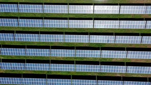 Solar panels aligned on green grass, showcasing renewable energy, aerial view