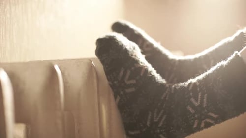 the Man Put His Cold Feet in Warm Woolen Socks on the Warm Radiator of the Home Heater