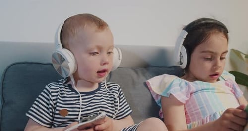 Children Wearing Headphones Using Phones on Couch