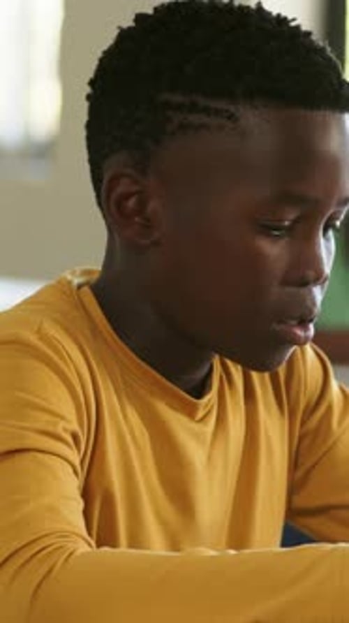 Vertical video: Seeing worksheet, student in mustard shirt leaning, reading and doing work at desk