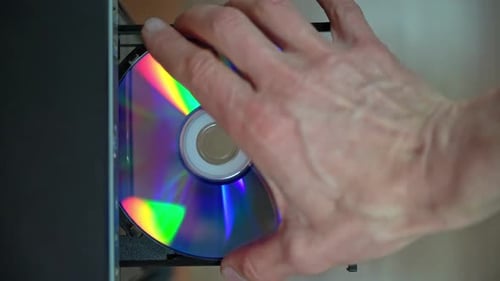 A male programmer takes out a CD-DVD from a computer drive.