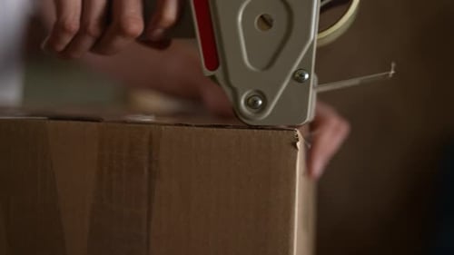 Warehouse Worker Sealing Cardboard Box with Tape Gun Ensuring Secure Packaging for Shipping Male
