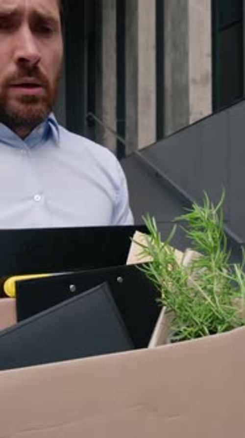 Gestresster entlassener kaukasischer Geschäftsmann mittleren Alters, der sein Büro in der Stadt mit einer Entlassungsbox verlässt, traurig