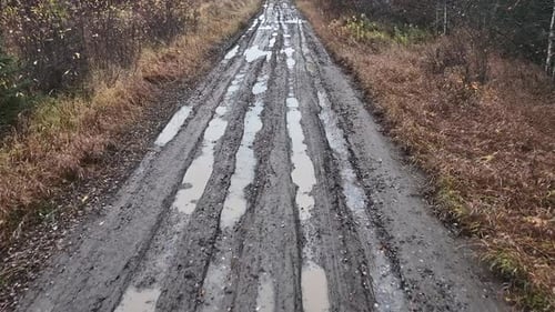 Drone moving down a very muddy and rutted up dirt road
