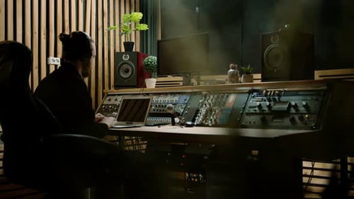 young sound engineer with headphones working in a music studio with monitors and an equalizer