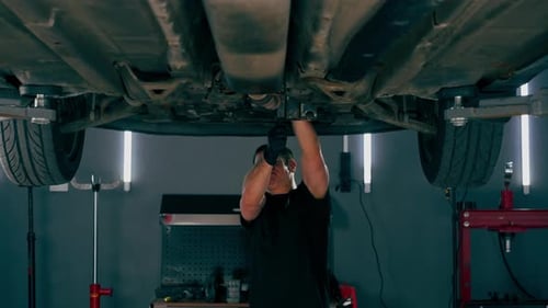 Ein Automechaniker an der Tankstelle überprüft ein Auto, das auf einem Aufzug angehoben wird, und behebt Probleme mit einem