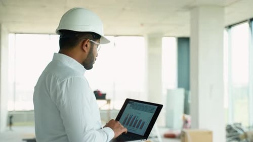 Indian Engineer Reviewing Construction Project Data with a Laptop Onsite