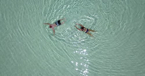 Bird eye view of a couple swimming together in crystal clear water of Maldives. The camera slowly ro