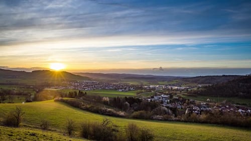 Dawn Illuminates a Town in a Hilly Valley with Forests and Meadows
