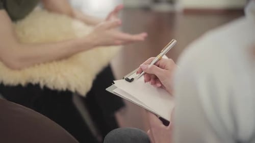 Man Gesturing While Woman Takes Notes on Clipboard