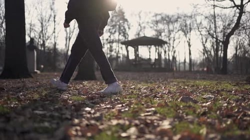 Lower shot of a young man walking alone in slow motion through a park full of fallen autumn leaves.