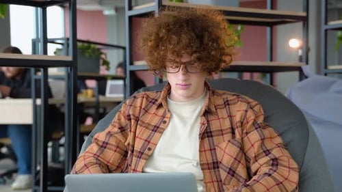 Young Student Freelancer Using Laptop and Listens to Music in Co Working Space