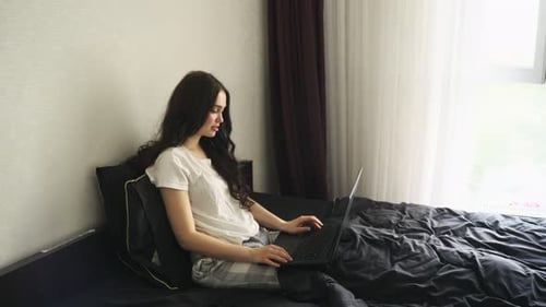 Lächelnde Frau genießt es, am Laptop zu arbeiten, während sie im Bett sitzt