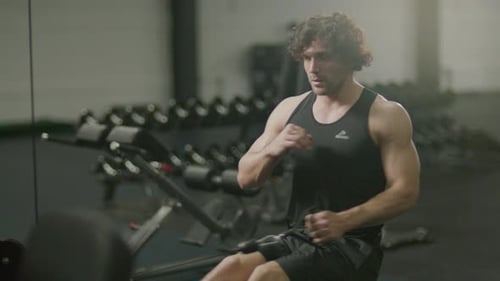 Muscular Man Working Out on Rowing Machine at Gym
