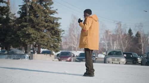 Documentarian Sipping Drink While Walking Snowy City Street Under Winter Sun