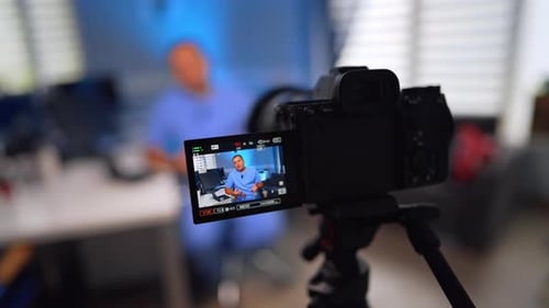 Caucasian doctor in blue uniform sits at desk talking. Medic creates a video vlog in his office.