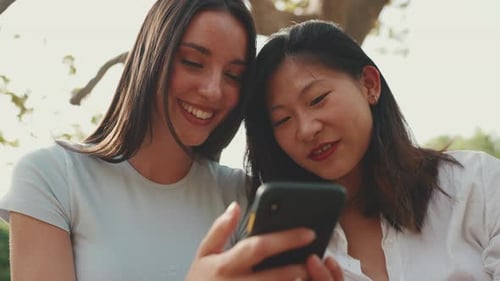 Smiling Friends Look at Phone in Park