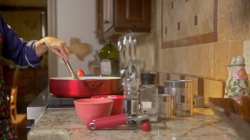 Slider reveals woman stirring food cooking in a pan on the stove