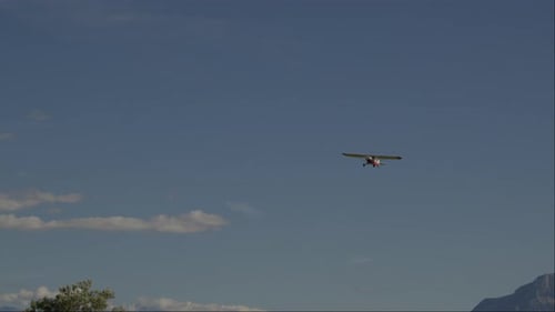 Small Airplane Flying over Green Fields and Mountains