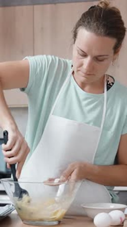 Verticale. Dans un intérieur de cuisine lumineux, une jeune femme remue la pâte à choux