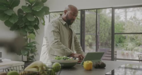 Man Preparing Salad Using Tablet in Kitchen