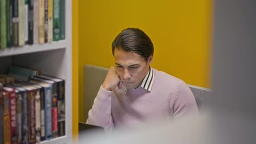 Joven concentrado que usa una computadora portátil mientras estudia en una biblioteca moderna