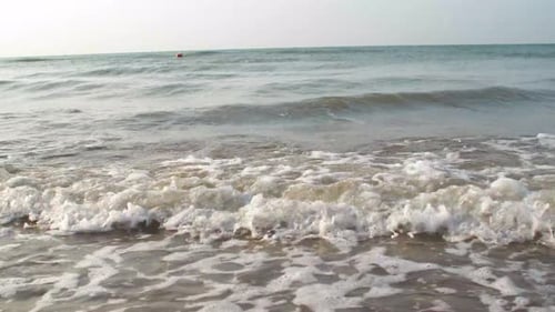 Kleine Wellen kommen an einem Sandstrand mit blauem Himmel herein.