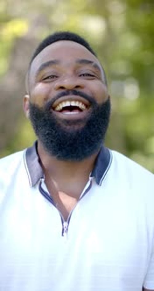 Vidéo verticale : Homme souriant à l'extérieur profitant d'une journée ensoleillée, vêtu d'un polo blanc