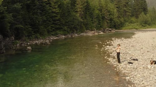 Man fly fishing with dog at a shallow river in McDonald Creek, wide drone tracking shot