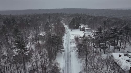 Aerial birds eye shot over snowy street in woodland of USA. Single family houses and homes in suburb