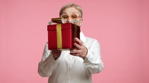 Senior Woman Presents Red Gift on Pink Background