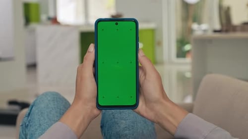 Womans Hands Holding Smartphone with Green Screen Laying on Sofa in Living Room