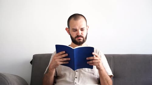 Man Reading a Book on a Grey Couch