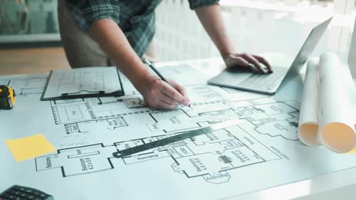 Interior designer or architect reviewing blueprints and holding pencil drawing on desk
