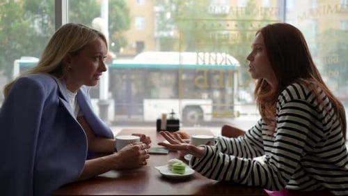 Vue latérale de deux jeunes amies heureuses assises dans un café en train de prendre un café et de discuter assises