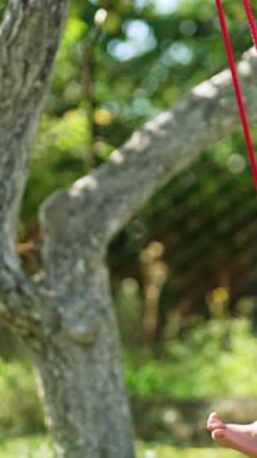 Lovely toddler swinging on a blue swing in the garden. Baby looking attentively into camera.