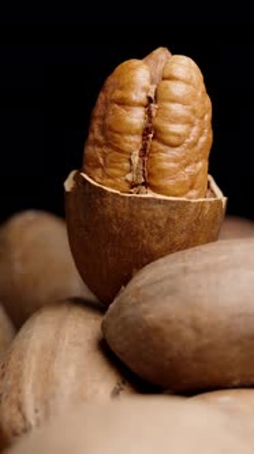 Vertical video. Half of a peeled pecan on top of a pile of nuts, close-up, rotating on a black
