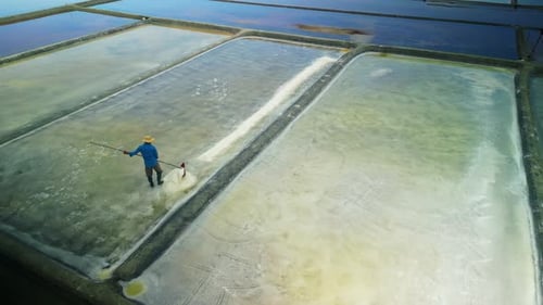 Asian Salt Worker Harvesting Crystals in Solar Evaporation Ponds Aerial View
