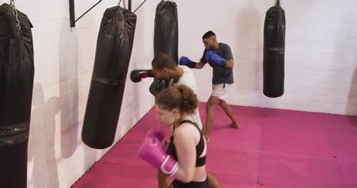 Diverse trainees guarding before heavy bags at gym, delivering jab-cross-hook drills for speed