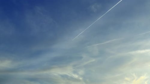 A Flying Airplane Leaves Contrails In A Beautiful Blue Sky With Clouds During The Day