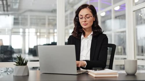 Businesswoman Smiles at Camera While Working on Laptop at Office Desk