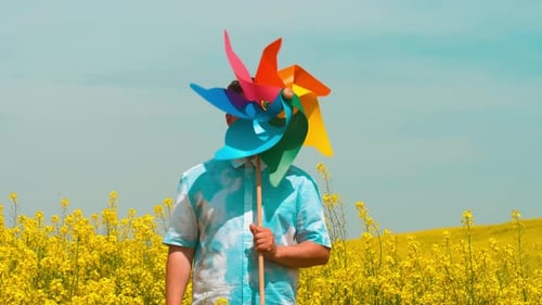 Caucasian man in sky with clouds print shirt in a rapeseed field with colorful pinwheel, Poland