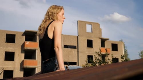 slow motion of a skinny blond woman model sitting on the edge of concrete wall and thoughtfully loo