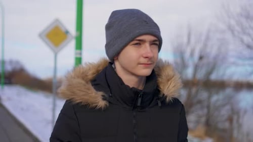 Handsome Boy Student Walks Along Snowy Road Street on Outskirts of City