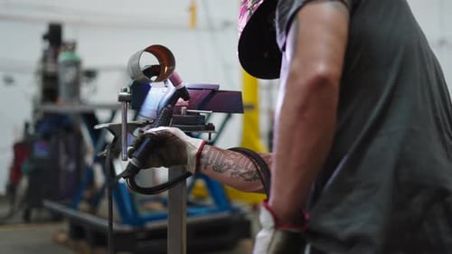 Professioneller Metallurg mit Tattoo beim Schweißen eines kreisförmigen Metallteils in einer Industriewerkstatt