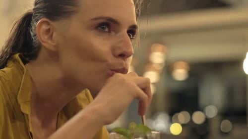 Young, Happy Woman Drinking Mohito Sitting in Bar at Night 30s